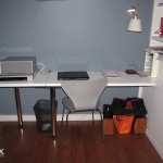 A desk with a fold up wing for a printer and white bookcases.